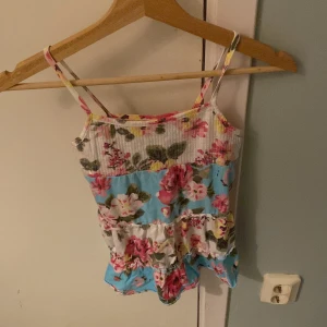 Blommig linnetopp från WETWEENS - Söt blommig linnetopp från WETWEENS med smala axelband. Toppen har ett färgglatt mönster i rosa, blått och grönt på en vit bas. Perfekt för varma sommardagar!