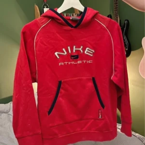 Röd hoodie från Nike - Säljer en röd hoodie från Nike med texten 'Nike Athletic' broderad på framsidan. Köpt secondhand men bara använd en gång av mig. Barnstorlek men passar mig som har storlek XXS-S