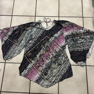 Mönstrad blus med vida ärmar från Louis, storlek M/L - Säljer en unik blus med ett färgglatt mönster i svart, rosa och beige. Blusen har vida ärmar och ett vackert blommönster med glittriga detaljer. Perfekt för att sticka ut i mängden!