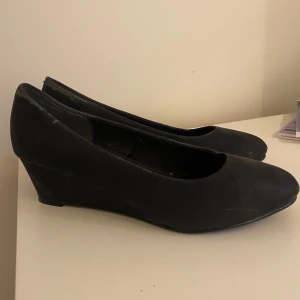Svarta kilklackskor - Säljer ett par svarta kilklackskor. Skorna har en rundad tå och klacken är ca 3 cm hög. Skorna har varit använda men inte alls många gånger. Säljer då de inte passar längre.