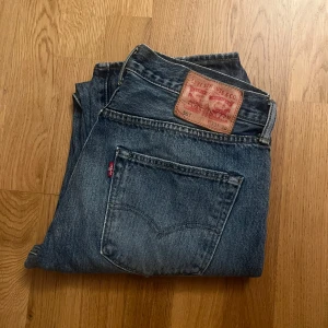 Blå jeans från Levi's 501 - Klassiska blå Levi's 501 jeans med en rak passform. De har en traditionell femficksdesign och en knappgylf. Perfekta för en avslappnad stil.    Storlek:                                                                                W:33 L:30