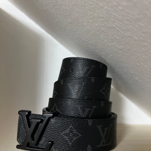 Lv bälte svart - Snyggt svart bälte från Louis Vuitton med det klassiska monogrammönstret och en stilren LV-spänne i svart. Tillverkat i Frankrike med en insida i ljusbrunt läder. Perfekt för att ge en lyxig touch till din outfit. 125cm vid frågor eller funderingar hör av er!