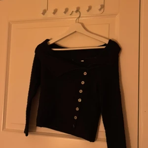 Svart stickad kofta med knappar - Säljer en svart stickad kofta med långa ärmar och knappar framtill. Koftan har en unik stickad struktur och en bred krage. Perfekt för att hålla sig varm och stilren.