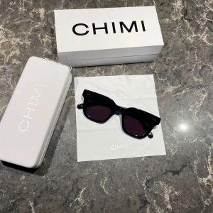 Svarta solglasögon från CHIMI - Snygga svarta solglasögon från CHIMI med en klassisk fyrkantig form. De har mörka linser och en robust båge som ger en stilren look. Perfekta för att ge din outfit en cool touch.