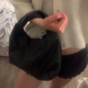 Svart handväska med flätat mönster - Snygg svart handväska med ett elegant flätat mönster. Perfekt för att ge din outfit en stilren touch. Väskan har en praktisk dragkedja för säker förvaring av dina saker.