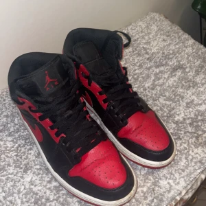 Nike Air Jordans i svart och rött - Snygga Nike Air Jordans i klassisk svart och röd färgkombination. Skorna har snörning och en ikonisk design med hög ankel. 