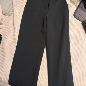 Svarta kostymbyxor - Snygga svarta kostymbyxor med hög midja och rak passform. Perfekta för en stilren look. Byxorna har diskreta fickor baktill och stängs med dragkedja och knapp framtill. Passar mig perfekt längdmässigt som är 169 cm lång. 