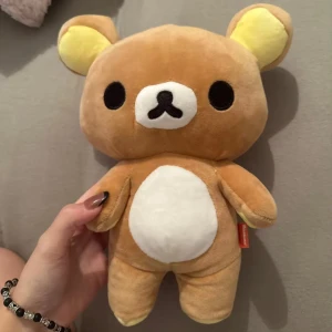 Rilakkuma mjukisdjur nyskick - Säljer en söt och mjuk Rilakkuma nallebjörn i ljusbrun färg med vita och gula detaljer. Den har en dragkedja på baksidan och är perfekt för alla som älskar japanska karaktärer. Perfekt som present eller för att dekorera rummet! Nyskick endast öppnad ur förpackningen för att fota den.