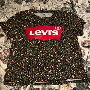 Blommig t-shirt från Levi's - Snygg blommig t-shirt från Levi's med det klassiska röda logotyptrycket på bröstet. Perfekt för en avslappnad stil med korta ärmar och en bekväm passform.