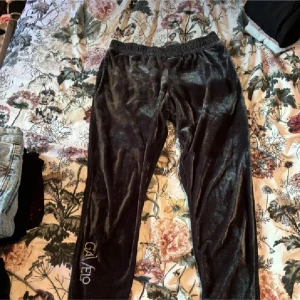 Svarta velourbyxor från Gavelo - Snygga svarta velourbyxor från Gavelo med elastisk midja för extra komfort. Byxorna har en stilren design med logotypen broderad längs benet. Perfekta för en avslappnad look.