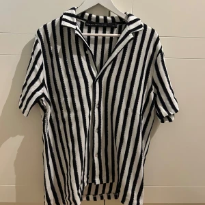 Svartvit randig skjorta - Snygg svartvit randig skjorta med korta ärmar och knappar framtill. Perfekt för en stilren look med en klassisk krage. Passar bra till både jeans och chinos.