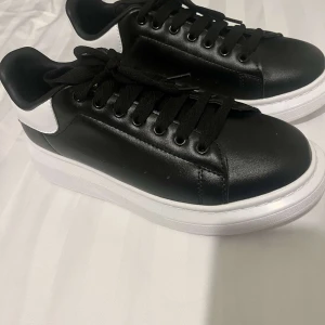 Svarta och vita sneakers från Alexander McQueen - Stilrena svarta sneakers med vita detaljer från Alexander McQueen. Skorna har en tjock vit sula och klassisk snörning. Perfekta för en trendig look.