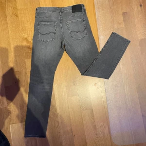 Grå Jack and Jones jeans - Snygga grå jeansbyxor med en slim passform. De har en klassisk femficksdesign och är perfekta för en stilren look. Modellen "Slim glenn". W29 L30. Priset är inte hugget i sten.