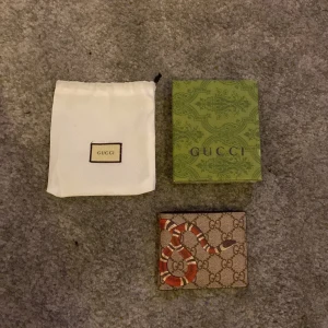 Gucci plånbok med ormmönster - Snygg Gucci plånbok med ikoniskt ormmönster på utsidan. Plånboken har flera kortfack och är tillverkad i skinn. Perfekt för den stilmedvetna som vill ha något unikt och lyxigt.