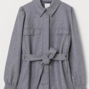 Grå kappa från H&M - Snygg grå kappa från H&M i hållbart italienskt tyg. Kappan har långa ärmar och ett bälte i midjan för en elegant look. Perfekt för höst och vår. Jag har använt den bara en gång och jag vill sälja den för att det är inte min stil så länge (storlek xs)
