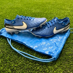 Blå Nike fotbollsskor - Snygga blå Nike fotbollsskor med vit sula och svart detaljering. Skorna har snörning och är perfekta för fotbollsplanen. De kommer med en matchande blå påse med Nike-logga. Dem är använda 1 gång och var för små. Nypris 3000 jag säljer för 2100 kr. Box och påse följer med. Hör av er vid frågor/ funderingar. 