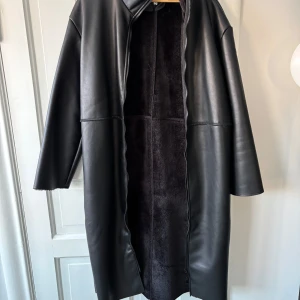 Svart lång kappa med fuskpälsfoder - Snygg svart lång kappa med fuskpälsfoder och dragkedja. Perfekt för kyliga dagar med sin stilrena design och långa ärmar. Ett måste för garderoben! Från NAKD, slutsåld