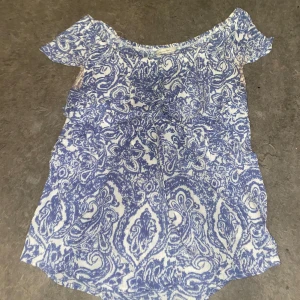 Blå och vit mönstrad blus - Säljer en blå och vit blus med ett detaljerat mönster. Blusen har korta ärmar och en rund halsringning. Perfekt för en somrig look!