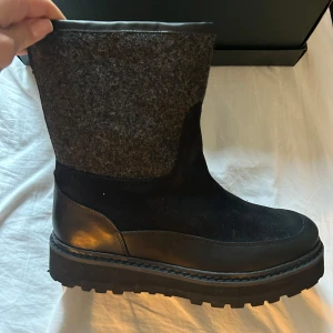 Svarta boots från Mono  - Snygga svarta boots från Mono med en robust sula och stilren design. Skorna har en kombination av skinn och ullmaterial, vilket ger en elegant och varm känsla. Perfekta för kyligare dagar. De är helt nya, aldrig använda och kommer med skokartong. Nypris är 3 299kr