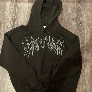 Svart hoodie från Weekday - Säljer en svart hoodie från Weekday med texten 'Spiritualism' i vitt på framsidan. Den har en klassisk design med huva och dragsko samt en stor magficka. Perfekt för en avslappnad stil.