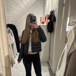 Svart pufferjacka från Mango - Snygg svart pufferjacka från Mango i en croppad stil. Jackan har långa ärmar och stängs med knappar. Perfekt för kyligare dagar när du vill hålla stilen.