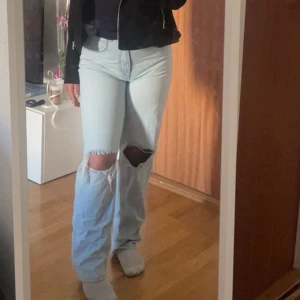 Ljusa jeans med slitningar - Säljer ett par ljusa jeans med stora slitningar på knäna. De har en loose passform och är högmidjade, vilket ger en avslappnad stil. Användt ett par gånger men ser helt nya ut