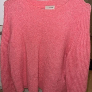 Rosa stickad tröja från By Malene Birger - Säljer en snygg rosa stickad tröja från By Malene Birger. Tröjan har en klassisk design med rund hals och långa ärmar. Perfekt för att hålla sig varm och stilren under kyligare dagar.