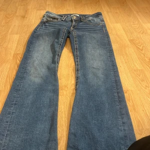 Blå jeans från Gina Tricot - Snygga blå jeans från Gina Tricot med bootcut-stil. De har klassisk femficksdesign och en knappgylf. Perfekta för en avslappnad look.