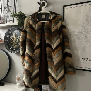 Flerfärgad pälsjacka - Säljer en cool flerfärgad pälsjacka med ett zigzag-mönster i brunt, beige och grått. Jackan har långa ärmar och en mysig, fluffig känsla. Perfekt för att sticka ut i mängden!