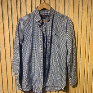 Blårutig skjorta från Ralph Lauren - Snygg blårutig skjorta från Ralph Lauren i slim fit. Skjortan har långa ärmar och knappar framtill samt en broderad logotyp på bröstet. Perfekt för en stilren look. Detta är en rutig skjorta från polo Ralph Lauren splitter nytt skick inga fel fläckar eller liknande. Den är rak i passformen och är som en ny skjorta skulle varit nypriset på denna är ungefär 1200 kr. Säljer denna nu för mycket lägre pris. Jag fraktar snabbt och den är storlek S. Ger en rutig stilren utseende och passar till event!