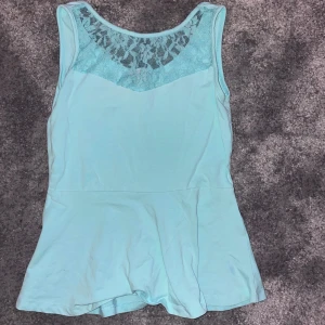Ljusblå ärmlös topp med spetsdetaljer - Snygg ljusblå ärmlös topp med spetsdetaljer vid halsringningen. Perfekt för varma dagar eller som ett lager under en jacka. Den har en luftig passform och är gjord i ett mjukt material.