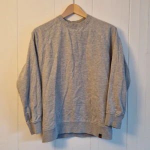 Grå sweatshirt från Denim Project - Stilren grå sweatshirt från Denim Project i storlek small. Tröjan har en klassisk design med rund hals och ribbade muddar vid ärmslut och nederkant.