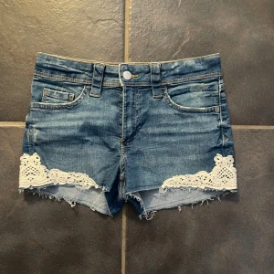Jeansshorts med spetsdetaljer från H&M - Snygga jeansshorts från H&M med spetsdetaljer vid benen. Perfekta för sommardagar med en avslappnad stil. De har en klassisk femficksdesign och fransiga kanter för en trendig look.