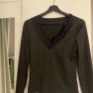 Svart långärmad topp med spetsdetaljer - Elegant svart topp med långa ärmar och v-ringad spetsdetalj. Perfekt för en stilren look. Aldrig använd! Vet inte var den är ifrån