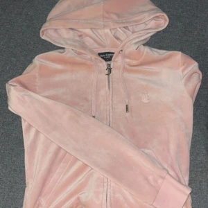Rosa kofta från Juicy Couture - Säljer en mjuk och stilren rosa hoodie från Juicy Couture. Den har dragkedja framtill och en liten broderad logga på bröstet. Perfekt för en avslappnad look.