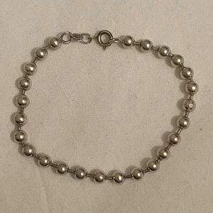 Silverfärgat armband med kulor - Elegant armband i silver med små, glänsande kulor. Armbandet har en klassisk design med en enkel låsning som gör det lätt att ta på och av. Perfekt för att ge en stilren touch till din outfit. Längd 19,5cm. Silver 925 stämplad.