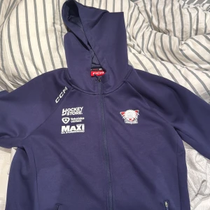 Mörkblå huvtröja från CCM - Säljer en mörkblå huvtröja från CCM med dragkedja och tryck på både fram- och bak. Använd 1 gång