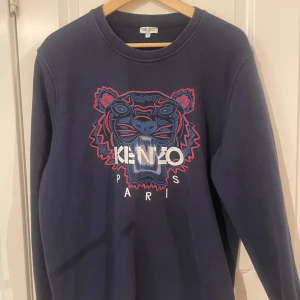 Mörkblå sweatshirt från Kenzo - Säljer en snygg mörkblå sweatshirt från Kenzo med ett coolt tigerbroderi och texten 'Kenzo Paris' på framsidan. Tröjan har långa ärmar och en rund halsringning. Perfekt för en stilren look.
