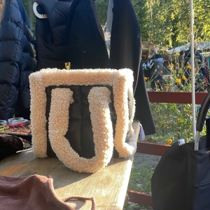 Svart och beige väska från Stand Studio - Säljer en superfin väska från Stand Studio! Den är svart med fluffiga vita detaljer som ger den en mysig look. Perfekt för höst och vinter. Väskan har en praktisk dragkedja upptill.