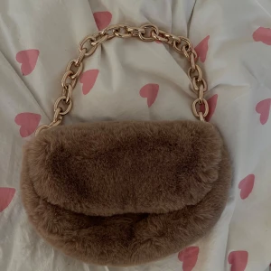 Brun pälsväska med kedjehandtag - Säljer en supermjuk och fluffig brun väska i pälsmaterial. Den har ett snyggt kedjehandtag i guld som ger en lyxig känsla. Perfekt för att piffa upp vilken outfit som helst! 👜✨