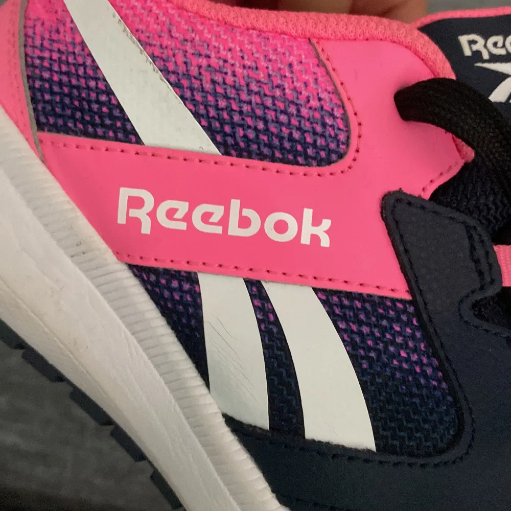 Säljer ett par snygga Reebok sneakers i blått och rosa. Skorna har en cool design med vita detaljer och svart snörning. De är i nyskick och perfekta för både träning och vardagsbruk. Storlek dam 37. Aldrig använd!. Skor.