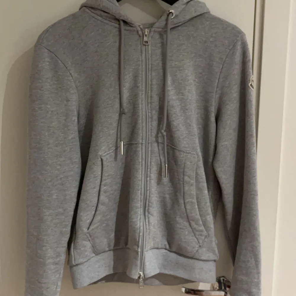 Säljer en snygg och bekväm grå hoodie från Moncler. Den har en dragkedja framtill och justerbara snören i huvan. Perfekt för en avslappnad stil och passar till alla tillfällen. Storlek S, i bra skick!. Fler bilder skriv. . Tröjor & Koftor.