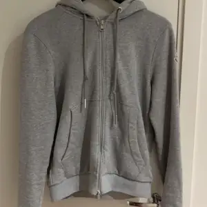 Säljer en snygg och bekväm grå hoodie från Moncler. Den har en dragkedja framtill och justerbara snören i huvan. Perfekt för en avslappnad stil och passar till alla tillfällen. Storlek S, i bra skick!. Fler bilder skriv. 