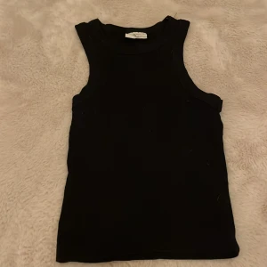 Svart linne från Gina  - Säljer en stilren svart ärmlös topp från Enjoy Basics i storlek XS. Perfekt för lager-på-lager eller att bära som den är under varma dagar. Toppen är i ett mjukt och bekvämt material, idealisk för både vardag och fest. Passar till allt!