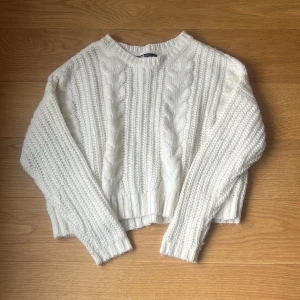 Vit stickad tröja - Mysig vit stickad tröja med kabelstickat mönster. Den är croppad och har långa ärmar, perfekt för kyliga dagar. Tröjan är i bra skick och passar både till vardags och lite finare tillfällen.