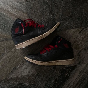 Svarta och röda Nike Air Jordans - Säljer ett par svarta Nike Air Jordans med röda detaljer och snörning. Skorna har en klassisk design med Air Jordan-loggan på sidan. De är i bra skick med lite slitage på sulan. Perfekta för både vardag och sportiga tillfällen!🖤❤️