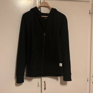 Svart ziphoodie från Jack & Jones - Säljer en stilren svart ziphoodie från Jack & Jones. Den har en dragkedja framtill och en praktisk huva med snören. Perfekt för både vardag och chill. Den är i bra skick och passar till alla tillfällen. Skön och enkel att matcha med andra plagg! Kostade 499 kronor