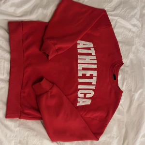 Röd sweatshirt från Gina Tricot - Säljer en snygg röd sweatshirt från Gina Tricot Den har ett stort vitt tryck på framsidan och är perfekt för en casual look. Tröjan har långa ärmar och ribbade muddar vid ärmslut och nederkant. Perfekt för höst och vår!