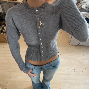 Grå ribbad kofta - Säljer en superfin grå kofta i ribbat material. Den är croppad och har en tight passform med knappar framtill. Perfekt för höst och vår, och funkar både till vardags och fest. Den har långa ärmar och en stilren look. Passar perfekt med jeans eller kjol!