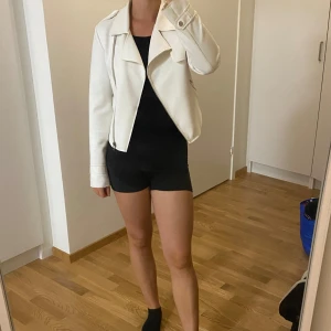 Vit skinnjacka i mjukt tyg - Säljer en snygg vit skinnjacka i mjukt tyg och mycket bra skick. Den har en klassisk bikerstil med dragkedja och långa ärmar. Perfekt för vår och höst, och funkar lika bra till fest som till vardags. Storleken är normal och den är superbekväm att ha på sig. Passa på att köpa denna stilrena jacka!